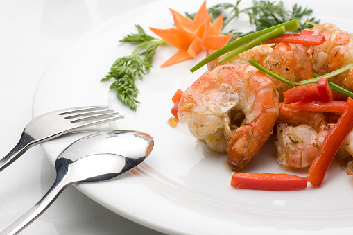 Shrimps with vegetables sautéed in olive oil, on a white square plate served at the table.