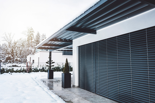 Contemporary building in winter time. Straight lines and monochrome colors give the house a strong modern feel. Design is simple and everlasting, big windows, making spaces bright on the inside. Hard roof top covering the terrace protecting it from snow.
