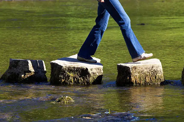 Photo of A person crossing three stepping stones on a river