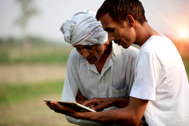 Agronomist consulting with farmer outdoor in the field Young agronomist Standing during sunset near green field with senior Farmer holding tablet computer & showing something in the tablet computer to the farmer. developing countries photos stock pictures, royalty-free photos & images