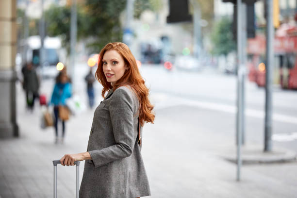 istock Young redhead woman with luggage on sidewalk 922594942
