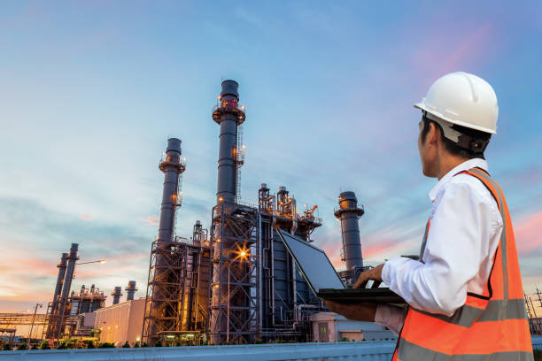 engineering utilizza il controllo del notebook e si trova di fronte alla struttura dell'edificio della raffineria di petrolio nell'industria petrolchimica pesante - factory site foto e immagini stock