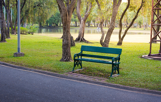 Green wooden long chair beside road in public garden with sunflare