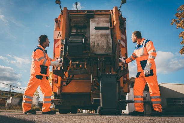 Two refuse collection workers loading garbage into waste truck stock photo