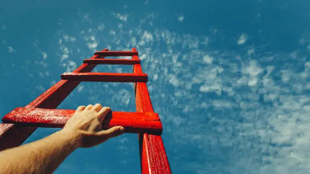 Photo of Development Attainment Motivation Career Growth Concept. Mans Hand Reaching For Red Ladder Leading To A Blue Sky