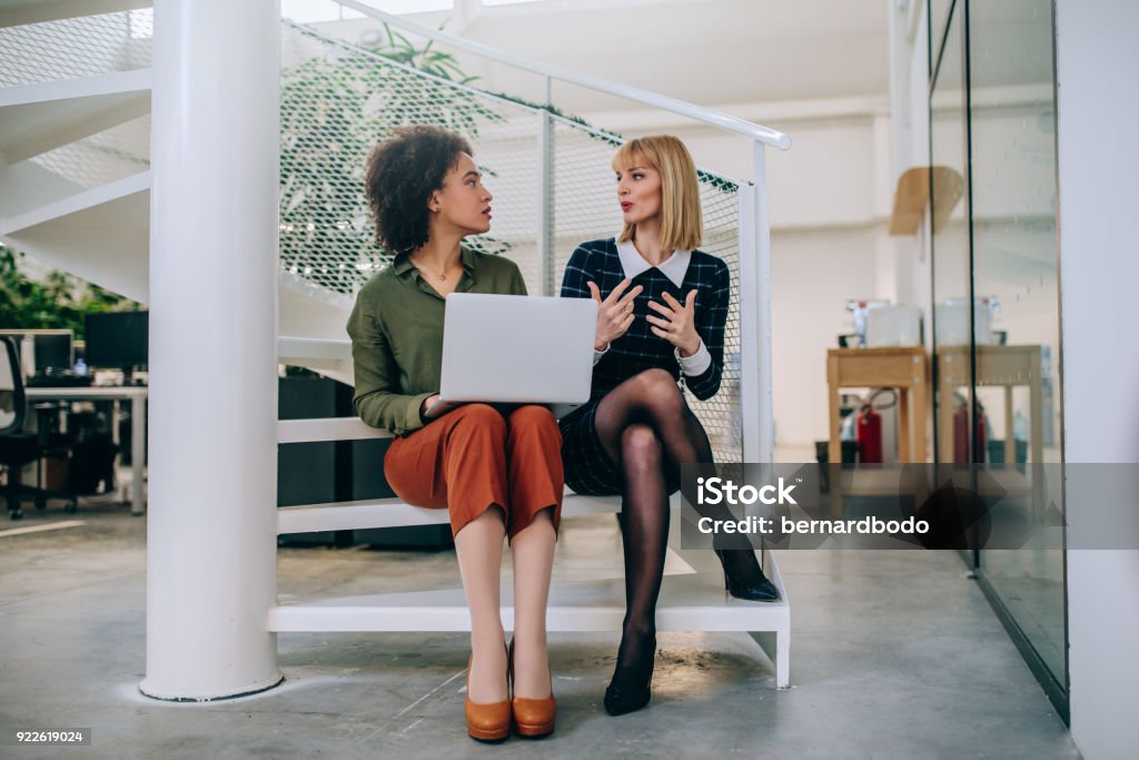Coming up with solution together Shot of two businesswomen sitting on the stairs talking Two People Stock Photo