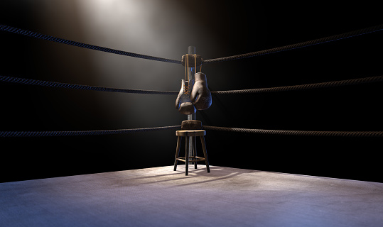A closeup of the corner of an old vintage boxing ring surrounded by ropes spotlit by a spotlight on an isolated dark background - 3D render