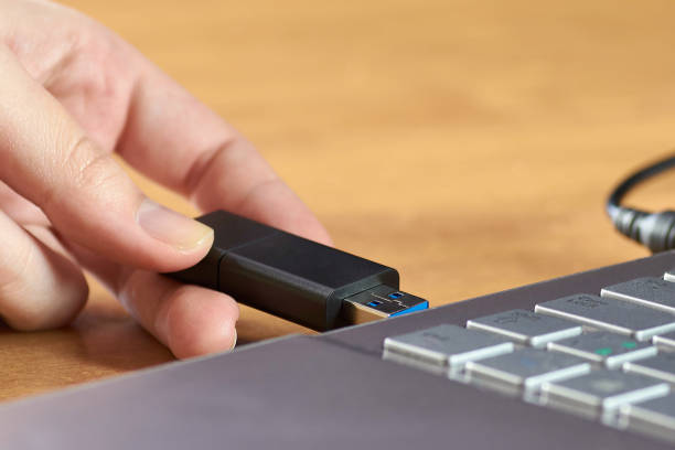 istock A female hand holding a USB flash drive before the silver laptop 922629334