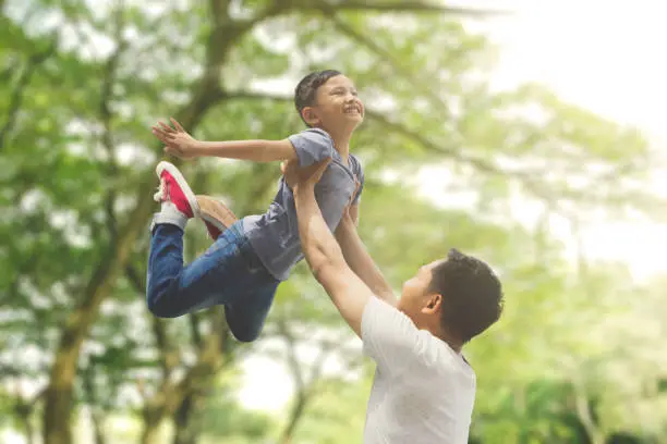 Asian family spending spring concept: a father lifting son with blur tree background