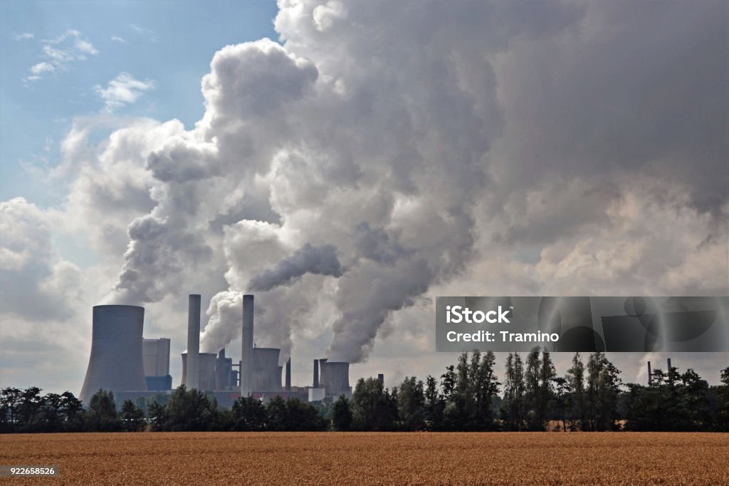 Factory chimneys emitting air pollutions Factory chimneys emitting air pollutions. View through the field on clouds of smoke and factory. Air Pollution Stock Photo