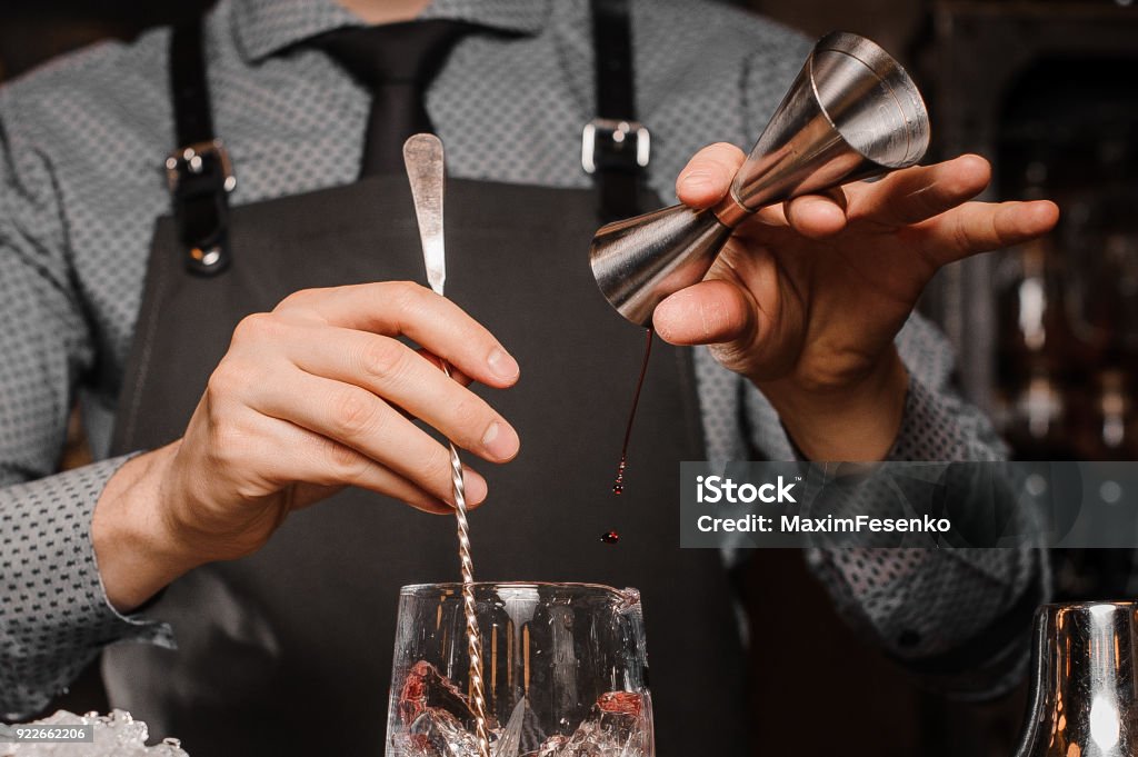 Barman in a shirt, tie and apron making an alcoholic drink Barman in a shirt, tie and apron making an alcoholic drink on the bar counter Cocktail Shaker Stock Photo