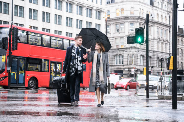 geschäftskollegen zu fuß in london straße mit schirm und koffer - london in the rain stock-fotos und bilder