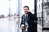 Mid adult businessman on cell phone in bus shelter with coffee