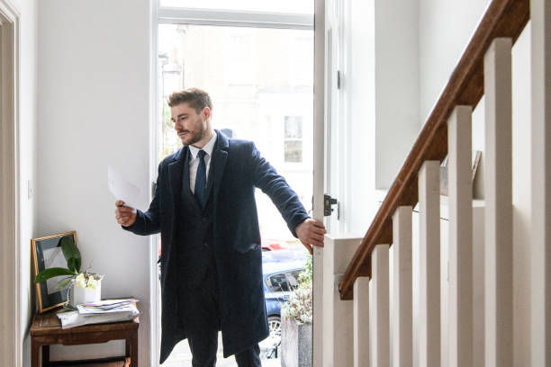 Businessman arriving home and checking post in hallway Mid adult man in suit coming back from work, opening front door and holding mail a letter returning home from work stock pictures, royalty-free photos & images