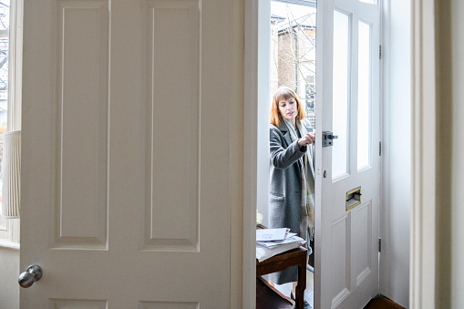 Businesswoman coming home at the end of the working day, view from inside house with internal door in foreground, woman seen through gap in front door