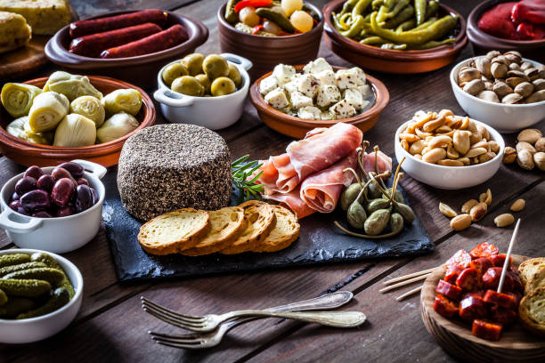 Tapas on rustic wooden table Wooden table filled with a large variety of spanish tapas. The composition includes spanish tortilla, pickles, cheese, chorizo, bread, peanuts, pistachios, salami, prosciutto, jalapeño peppers, anchovies and others. DSRL studio photo taken with Canon EOS 5D Mk II and Canon EF 100mm f/2.8L Macro IS USM salumeria stock pictures, royalty-free photos & images