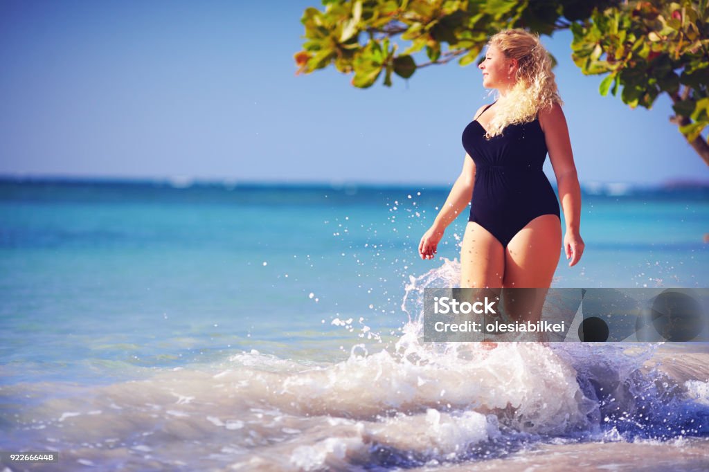 young plus size woman in swimwear enjoying vacation in water splash on the beach One Woman Only Stock Photo