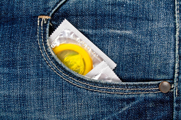 цветные презервативы в синем кармане джинсов - sexual issues aids condom human pregnancy стоковые фото и изображения