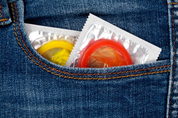 цветные презервативы в синем кармане джинсов - sexual issues aids condom human pregnancy стоковые фото и изображения