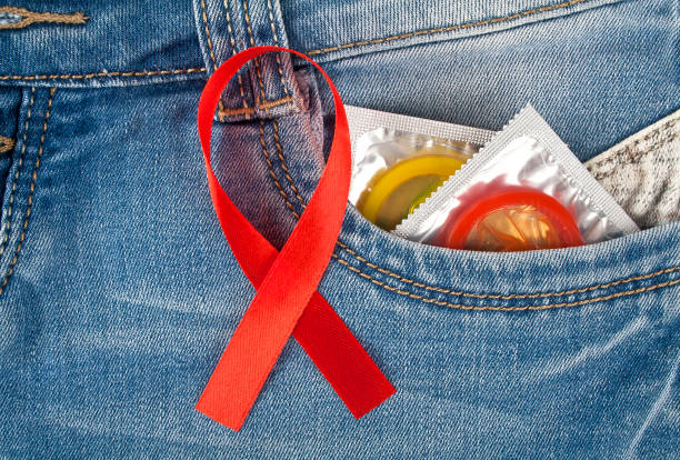 préservatifs colorés dans une poche de jeans bleu et le ruban rouge sida sensibilisation - sex condom jeans horizontal photos et images de collection