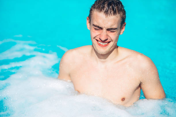 Young man rubbing eyes in swimming pool.Summer activity.Contact lens pollution, swimming in chlorine contaminated pool.Eyes burning in the pool.Allergy on chlorine chemical disinfection in water. stock photo
