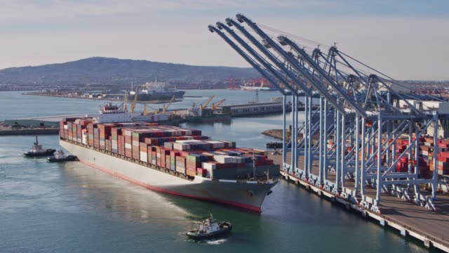 Tug Boats Manoeuvring Massive Cargo Ship Into Dock - Drone Shot