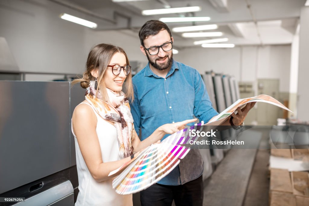 Woman with print operator at the manufacturing Young woman designer and print operator working together with color swatches standing at the print manufacturing Printing Plant Stock Photo