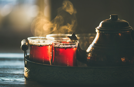 Traditional hot steaming Turkish tea in tulip glasses with copper pot in vintage tray