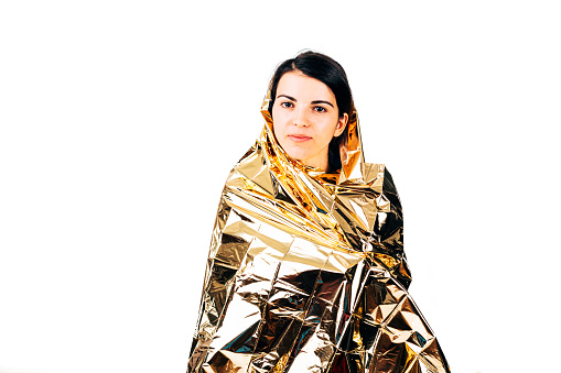 Closeup of a lost hiker woman wrapped on golden survival blanket- isolated on white.