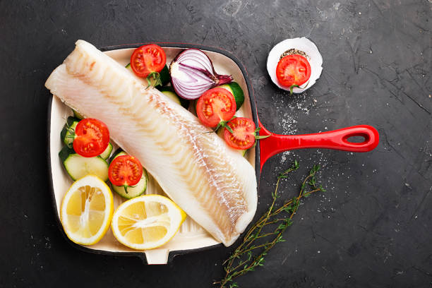 タラ。新鮮な海新鮮な野菜をフライパンで調理する前に生の魚の白: ズッキーニ、甘い玉ねぎ、トマト、レモン。平面図です。食品のコンセプト - sweet onion ストックフォトと画像