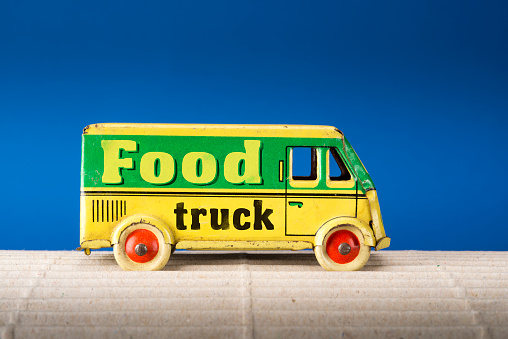 Food truck, vintage tin toy van on blue background.