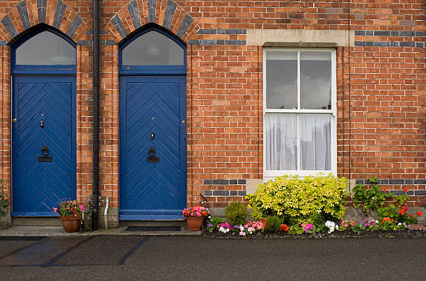 Charming facade of a traditional english house featuring a blue door and bay windows, with a garden in the foreground