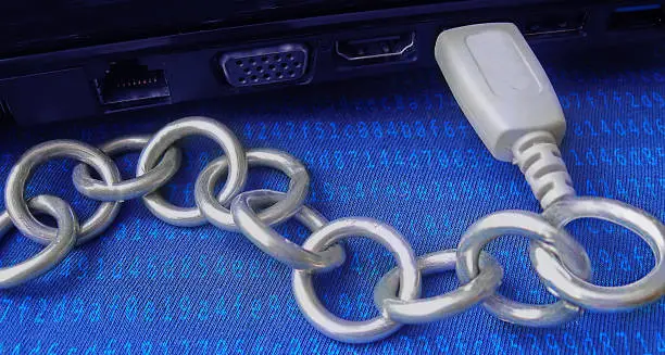 Blockchain technology is shown as a real metal chain joined by USB to a computer. Blue background covered with coded hash algorithm. Banner, header or poster is to illustrate information technology content