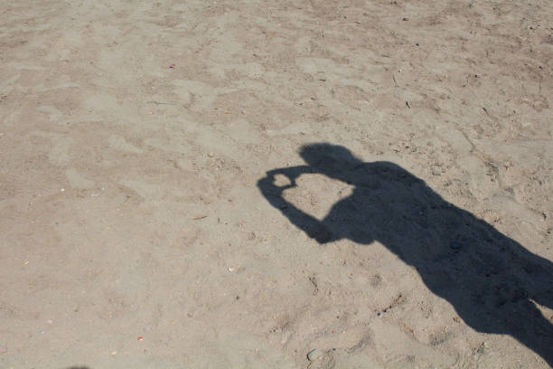 Shadow of man doing love sign on sand background.