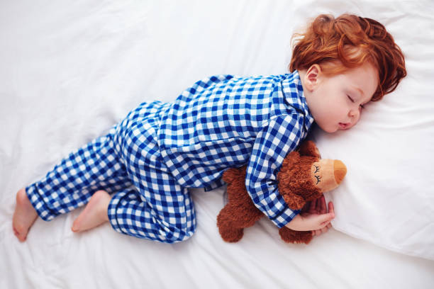 bébé de bébé adorable rousse dormir avec un jouet en peluche en pyjama de flanelle - baby sleeping bed babies only photos et images de collection