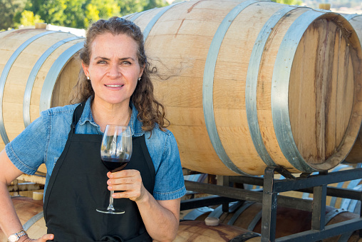 Mature caucasian woman holding a glass of wine with wine barrels in the background