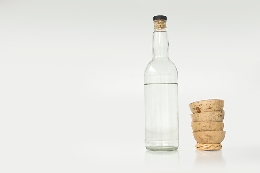 Isolated horizontal photo of a Mezcal bottle and a traditional piled up cups with white background.