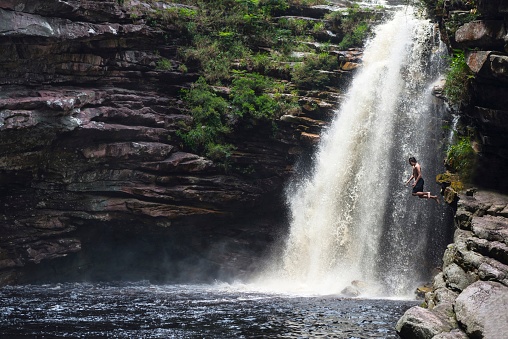 A boy jumping from a rock beside a waterfall in a wild ambience