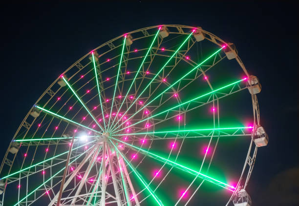 Bright Twisting Ferris Wheel Carnival ride showing spinning ferris wheel in action- long exposure shot. dar vueltas stock pictures, royalty-free photos & images