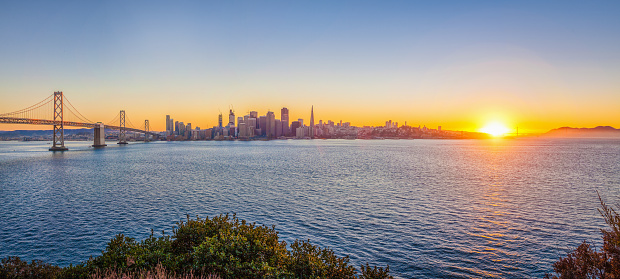 Classic panoramic view of San Francisco skyline with famous Oakland Bay Bridge illuminated in beautiful golden evening light at sunset in summer, San Francisco Bay Area, California, USA