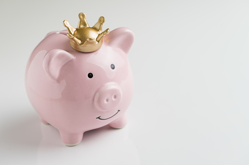 Financial winner or king of money savings concept, smiling happy pink piggy bank wearing a golden crown on top on seamless white table background, best future investment, compound interest deposit.