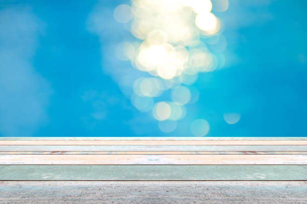 istock Perspective wood table top and Soft focus bokeh light effects over a rippled, blue water background in the pool 922728062
