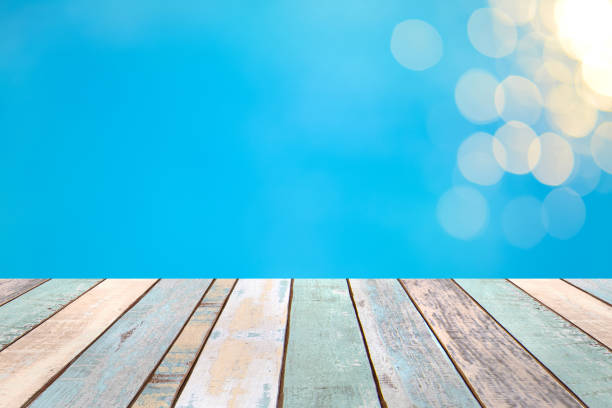 istock Perspective wood table top and Soft focus bokeh light effects over a rippled, blue water background in the pool 922728262