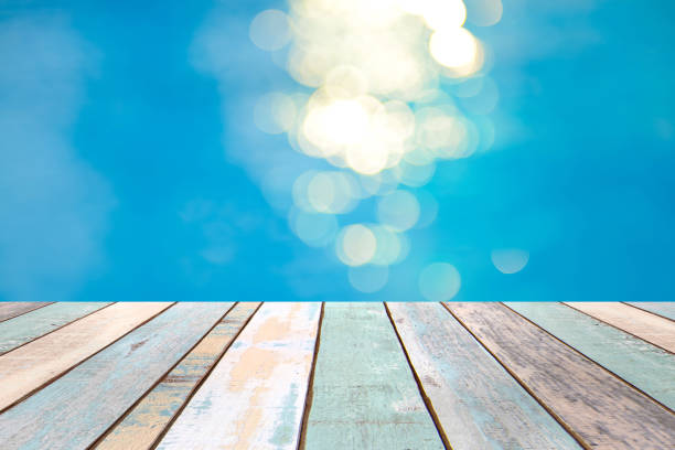 istock Perspective wood table top and Soft focus bokeh light effects over a rippled, blue water background in the pool 922728270