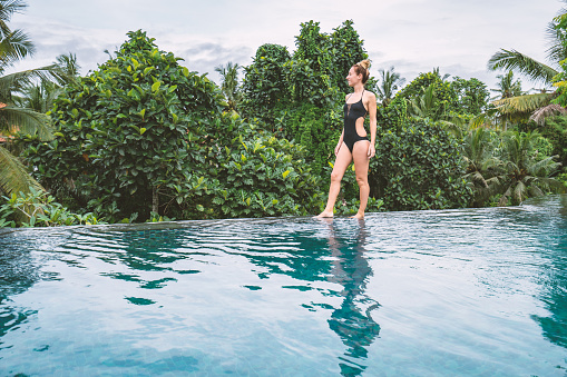 Young woman standing on the edge of an infinity pool, Ubud, Bali