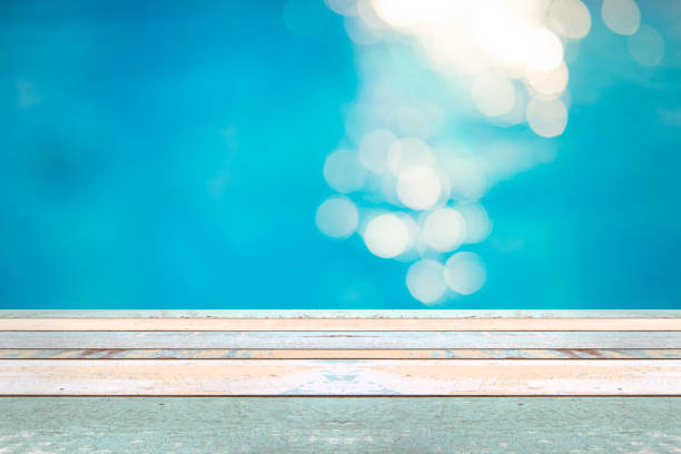 istock Perspective wood table top and Soft focus bokeh light effects over a rippled, blue water background in the pool 922728454