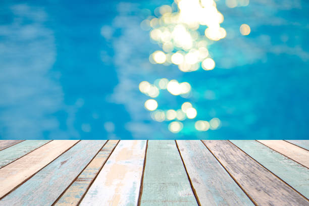 istock Perspective wood table top and Soft focus bokeh light effects over a rippled, blue water background in the pool 922728546