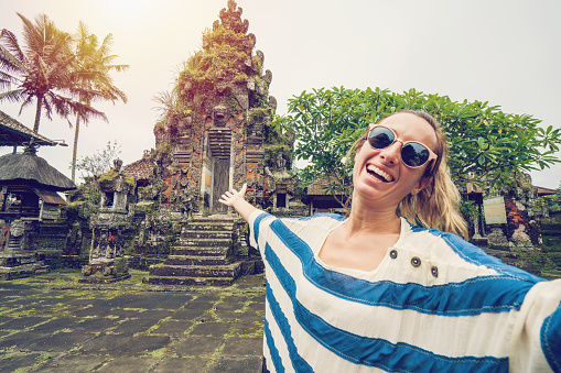 Caucasian young woman takes selfie with ancient temple in the lush greenery. People travel concept.