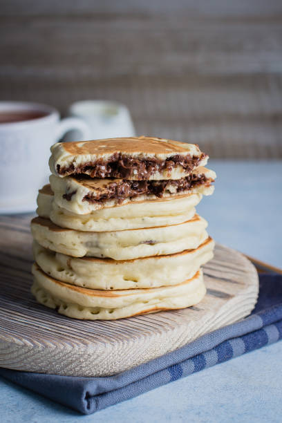 istock Stack of Stuffed chocolate nutella pancakes on vintage wooden board on blue table background with cup of tea. American Breakfast Concept. Copy space 922733692