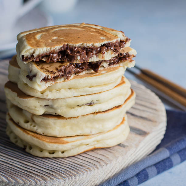istock Stack of Stuffed chocolate nutella pancakes on vintage wooden board on blue table background with cup of tea. American Breakfast Concept. Copy space 922733694